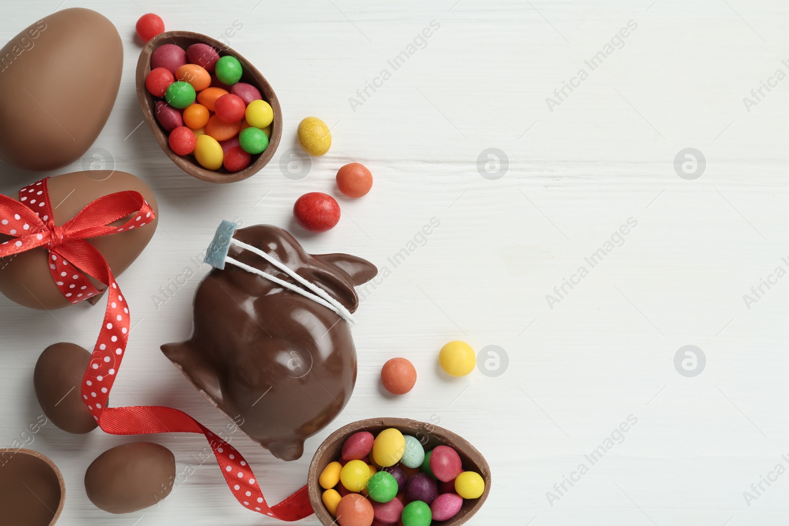Photo of Chocolate bunny with protective mask, eggs and space for text on white wooden table, flat lay. Easter holiday during COVID-19 quarantine
