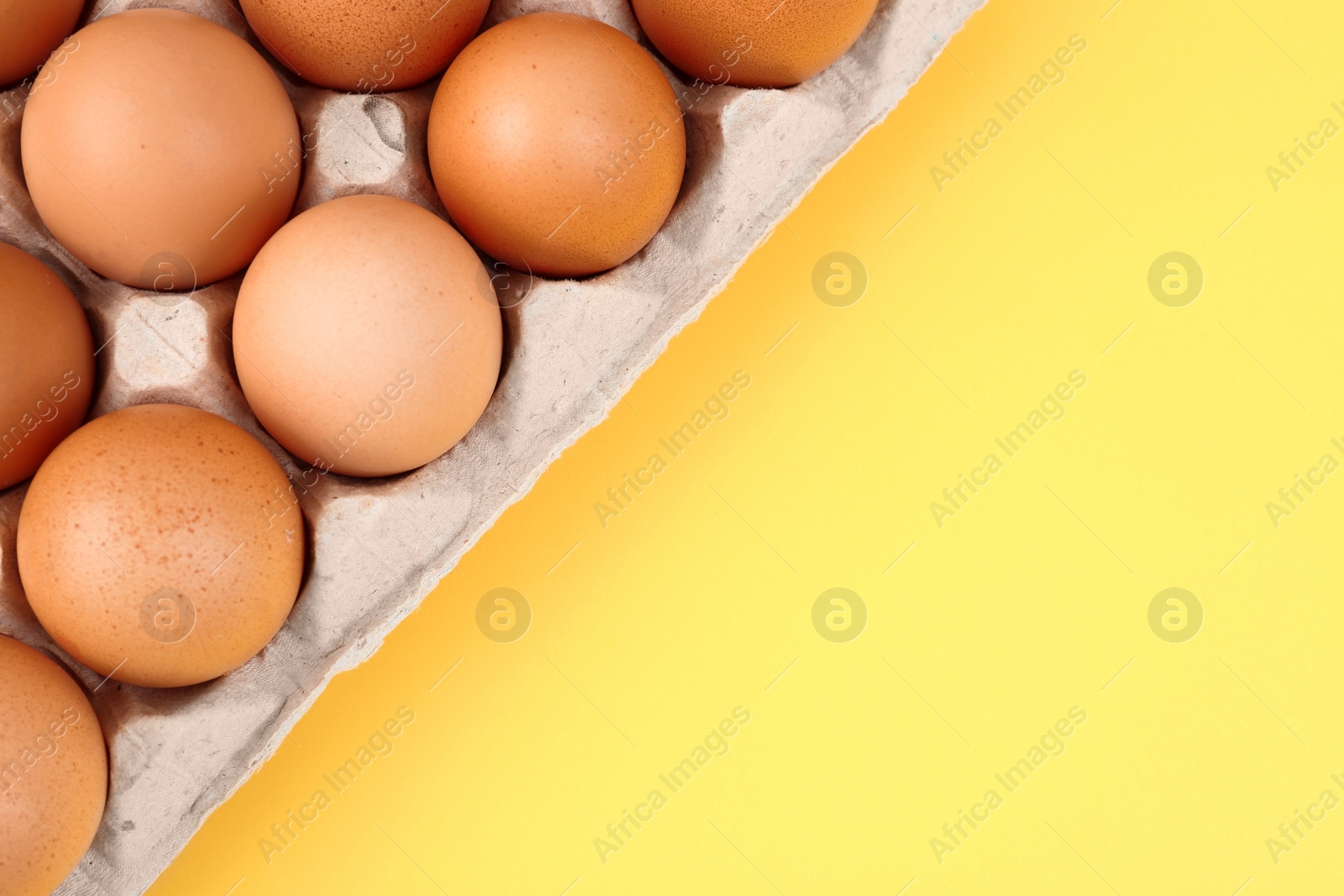 Photo of Raw chicken eggs on yellow background, top view. Space for text