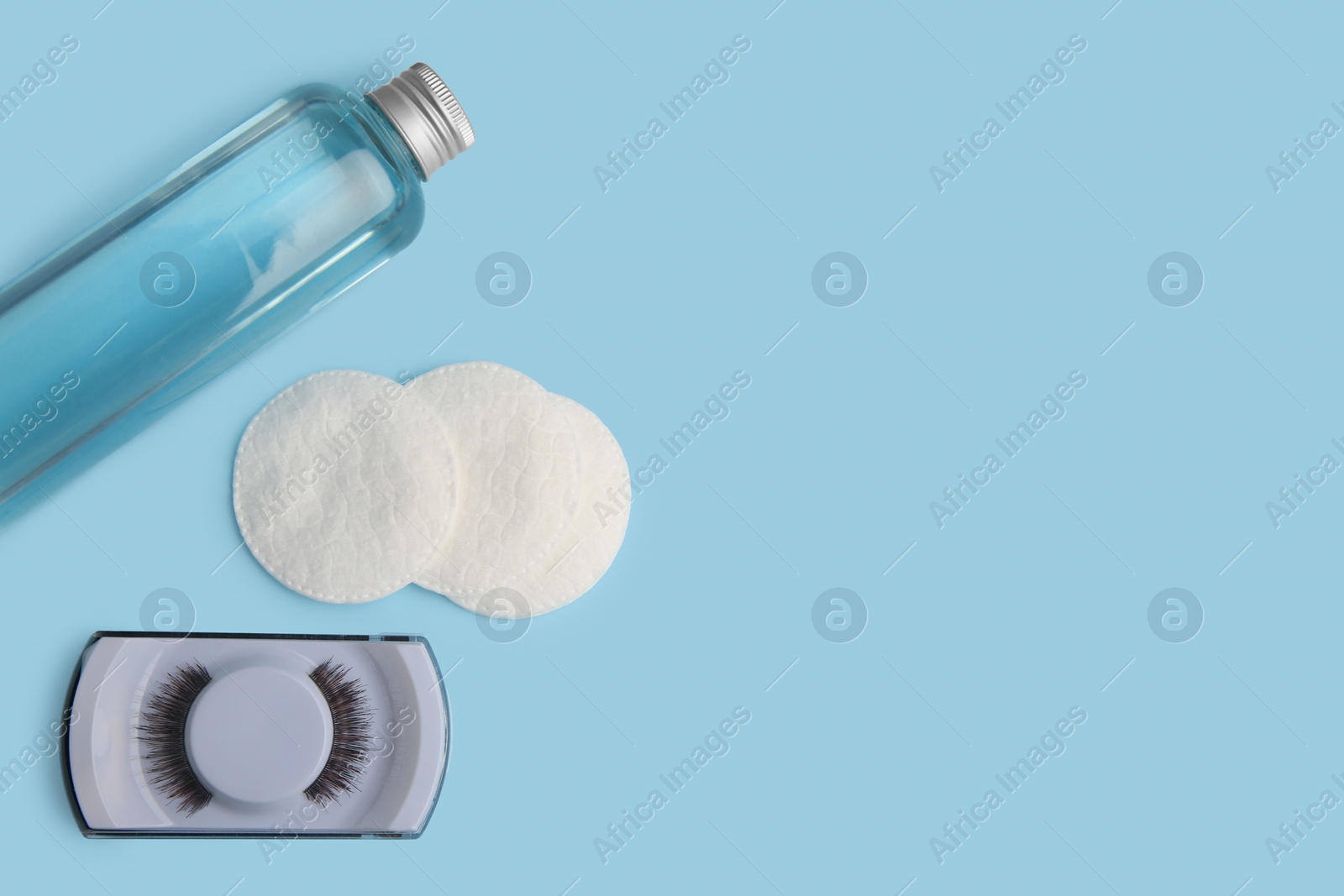 Photo of Bottle of makeup remover, cotton pads and false eyelashes on light blue background, flat lay. Space for text