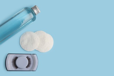 Bottle of makeup remover, cotton pads and false eyelashes on light blue background, flat lay. Space for text