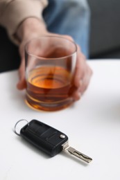 Photo of Man holding glass of alcoholic drink at table with car keys, closeup. Don't drink and drive concept