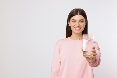 Healthy habit. Happy woman holding glass with fresh water on light grey background. Space for text