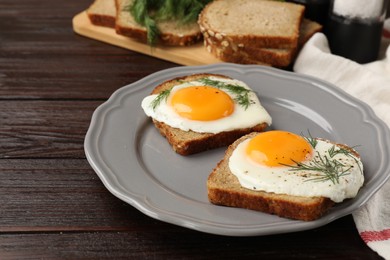 Photo of Plate with tasty fried eggs, slices of bread and dill on dark wooden table. Space for text