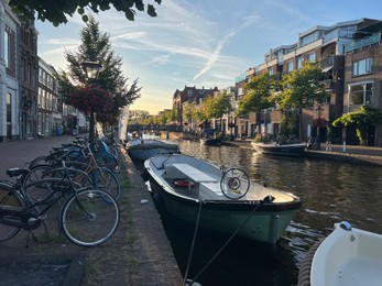 Photo of Leiden, Netherlands - August 1, 2022: Picturesque view of city canal with moored boats and parked bicycles