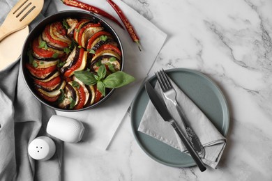 Delicious ratatouille, chili peppers and cutlery on white marble table, flat lay