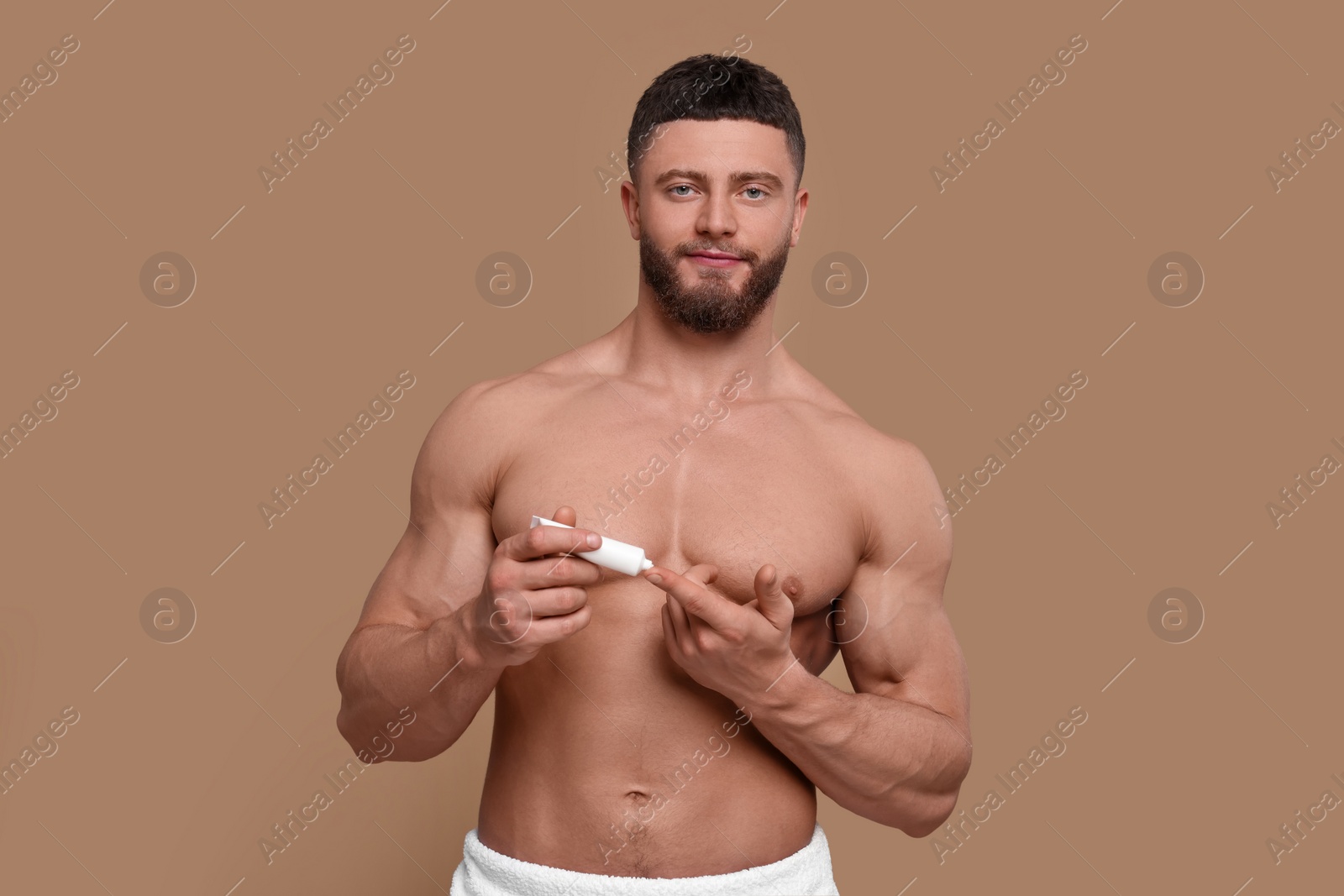 Photo of Handsome man applying body cream on pale brown background
