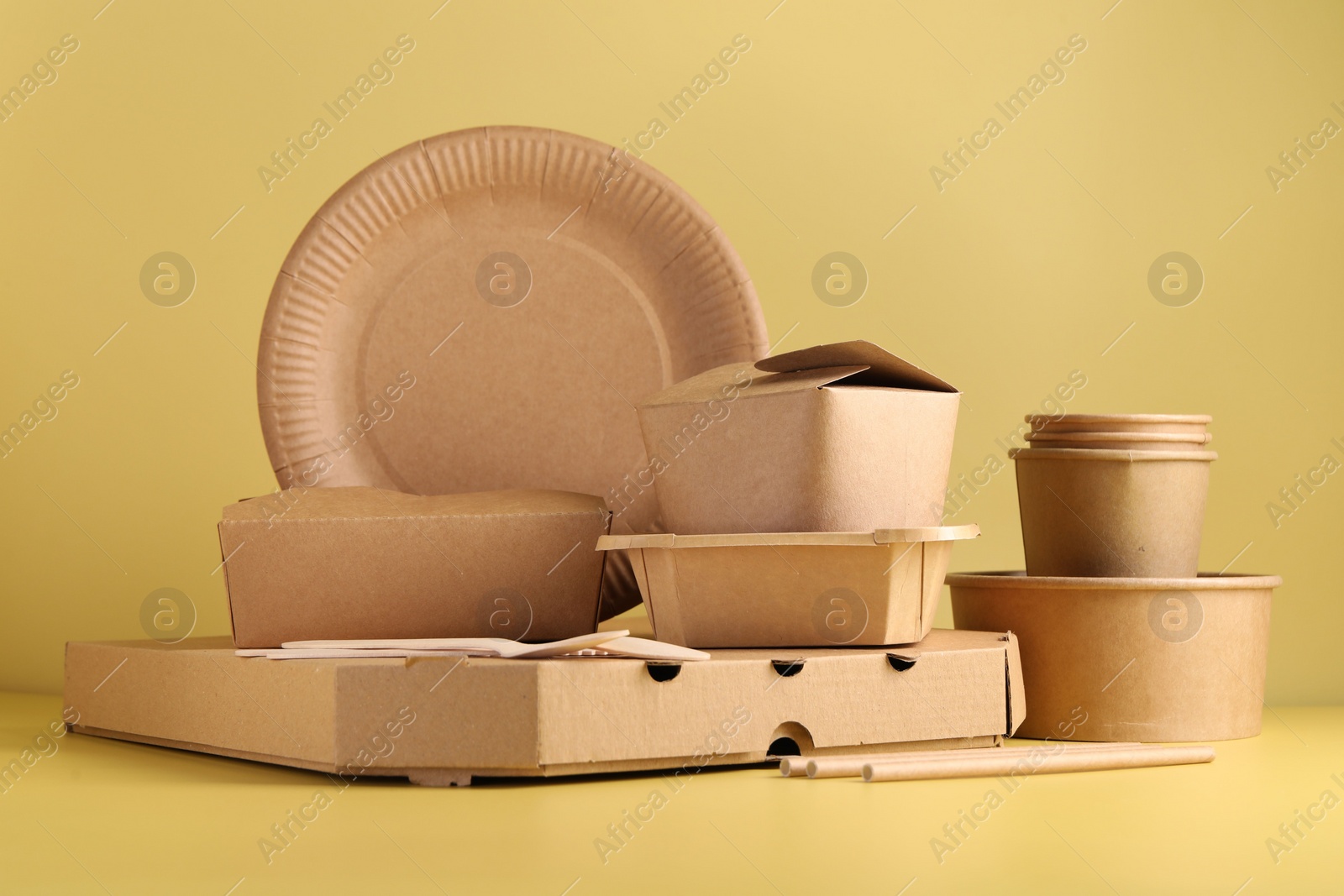 Photo of Eco friendly food packaging. Paper containers and tableware on pale yellow background