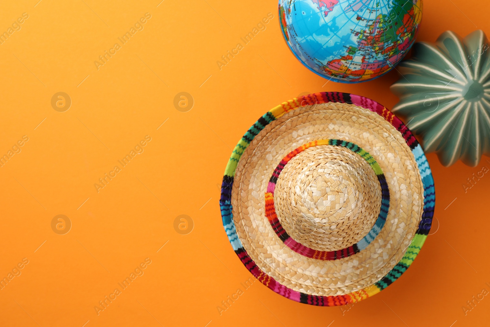 Photo of Mexican sombrero hat, globe and ceramic cactus on orange background, flat lay. Space for text