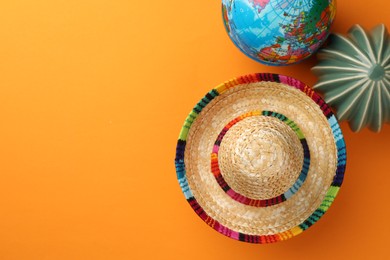 Mexican sombrero hat, globe and ceramic cactus on orange background, flat lay. Space for text