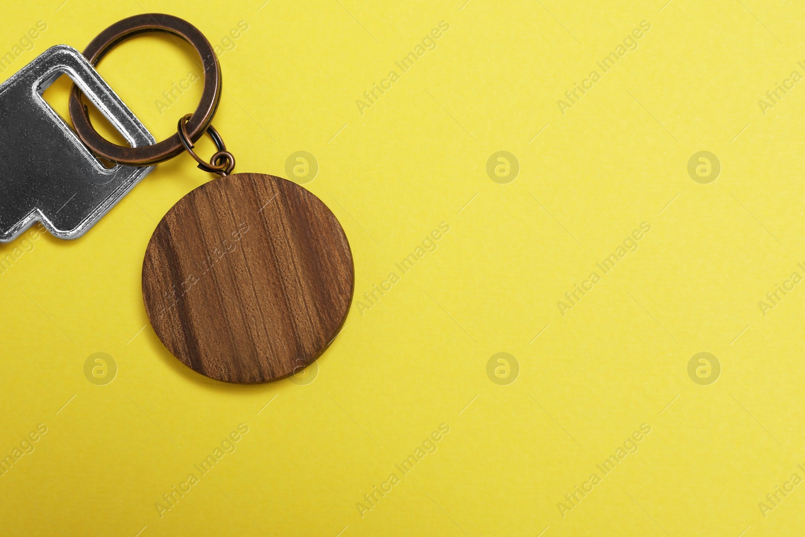 Photo of Key with wooden keychain in shape of house on yellow background, top view. Space for text