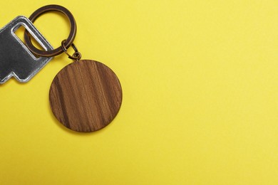 Photo of Key with wooden keychain in shape of house on yellow background, top view. Space for text