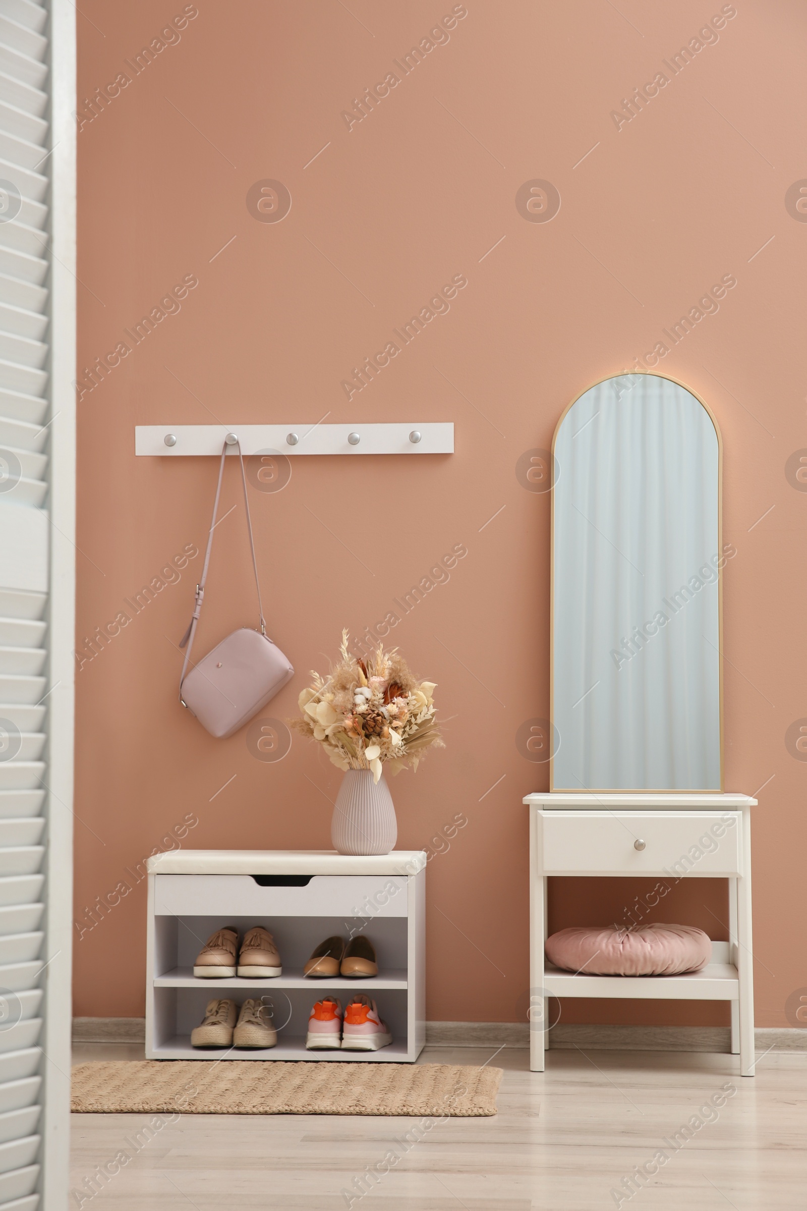 Photo of Hallway interior with mirror and white furniture near light pink wall. Stylish accessories