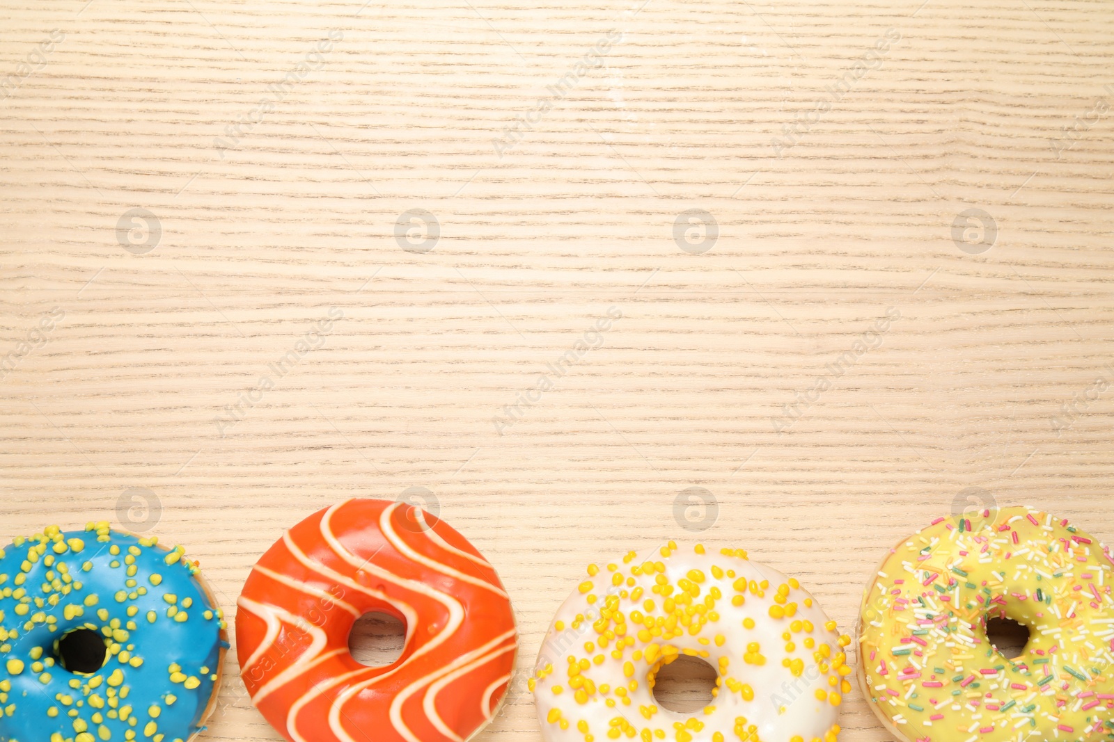 Photo of Delicious glazed donuts on wooden table, flat lay. Space for text