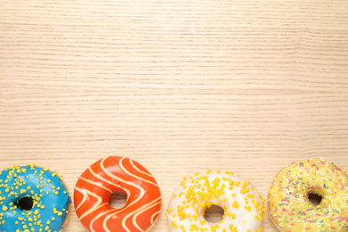 Photo of Delicious glazed donuts on wooden table, flat lay. Space for text