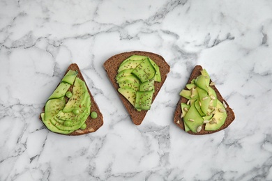 Tasty crisp rye toasts with avocado on marble table, top view