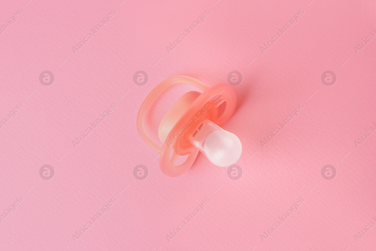 Photo of New baby pacifier on pink background, top view