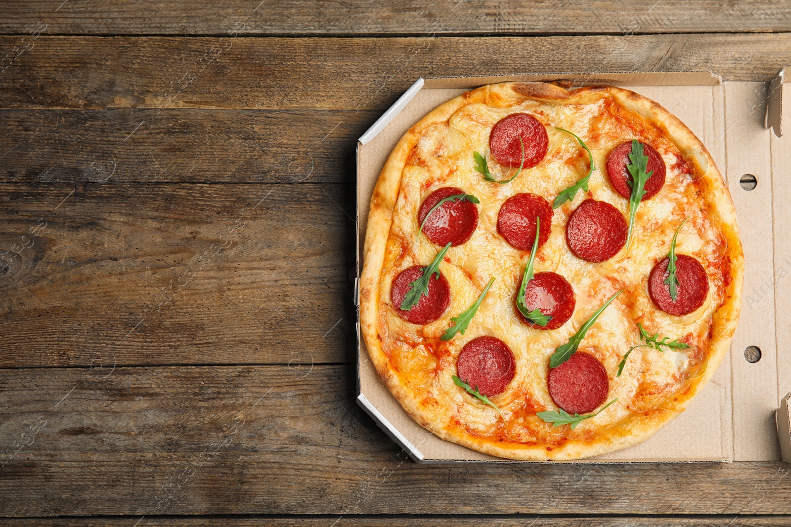 Photo of Tasty pepperoni pizza in cardboard box on wooden table, top view. Space for text