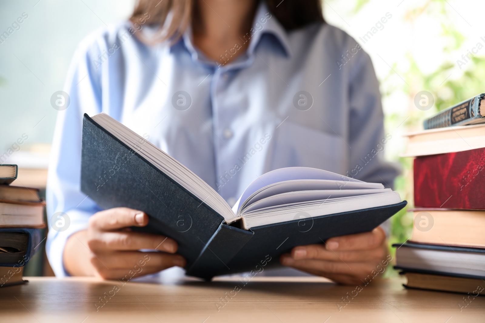 Photo of Woman reading hardcover book at wooden table indoors, closeup