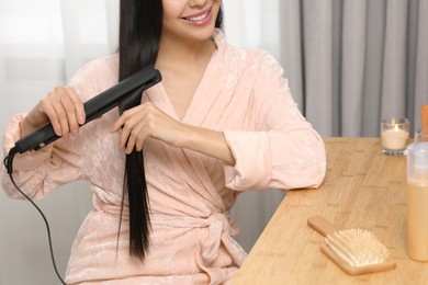 Photo of Woman using hair iron in room, closeup