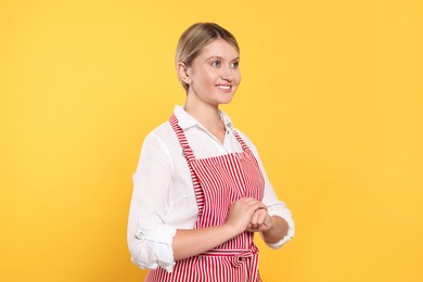 Beautiful young woman in clean striped apron on orange background