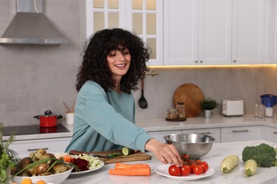 Photo of Woman cooking healthy vegetarian meal at white marble table in kitchen