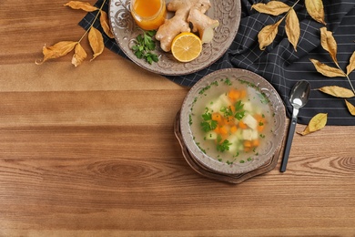 Flat lay composition with bowl of fresh homemade soup to cure flu and space for text on wooden background