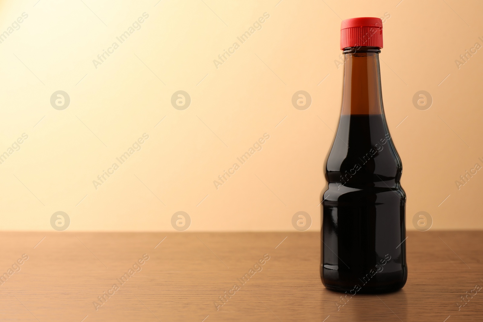 Photo of Bottle of soy sauce on wooden table against beige background. Space for text