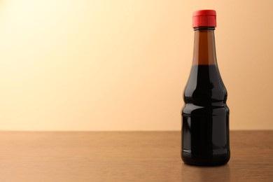 Photo of Bottle of soy sauce on wooden table against beige background. Space for text