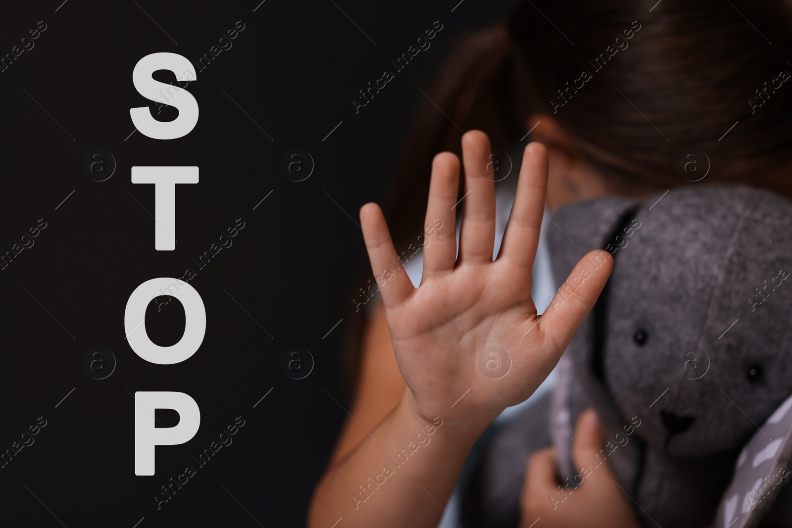 Image of No child abuse. Little girl with toy bunny making stop gesture on dark background, selective focus