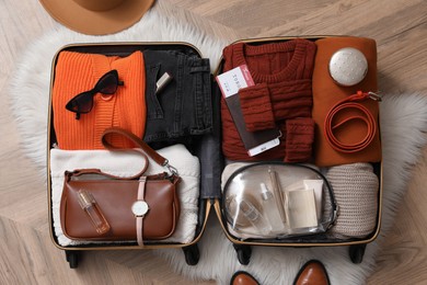 Photo of Open suitcase with folded clothes and accessories on floor, flat lay