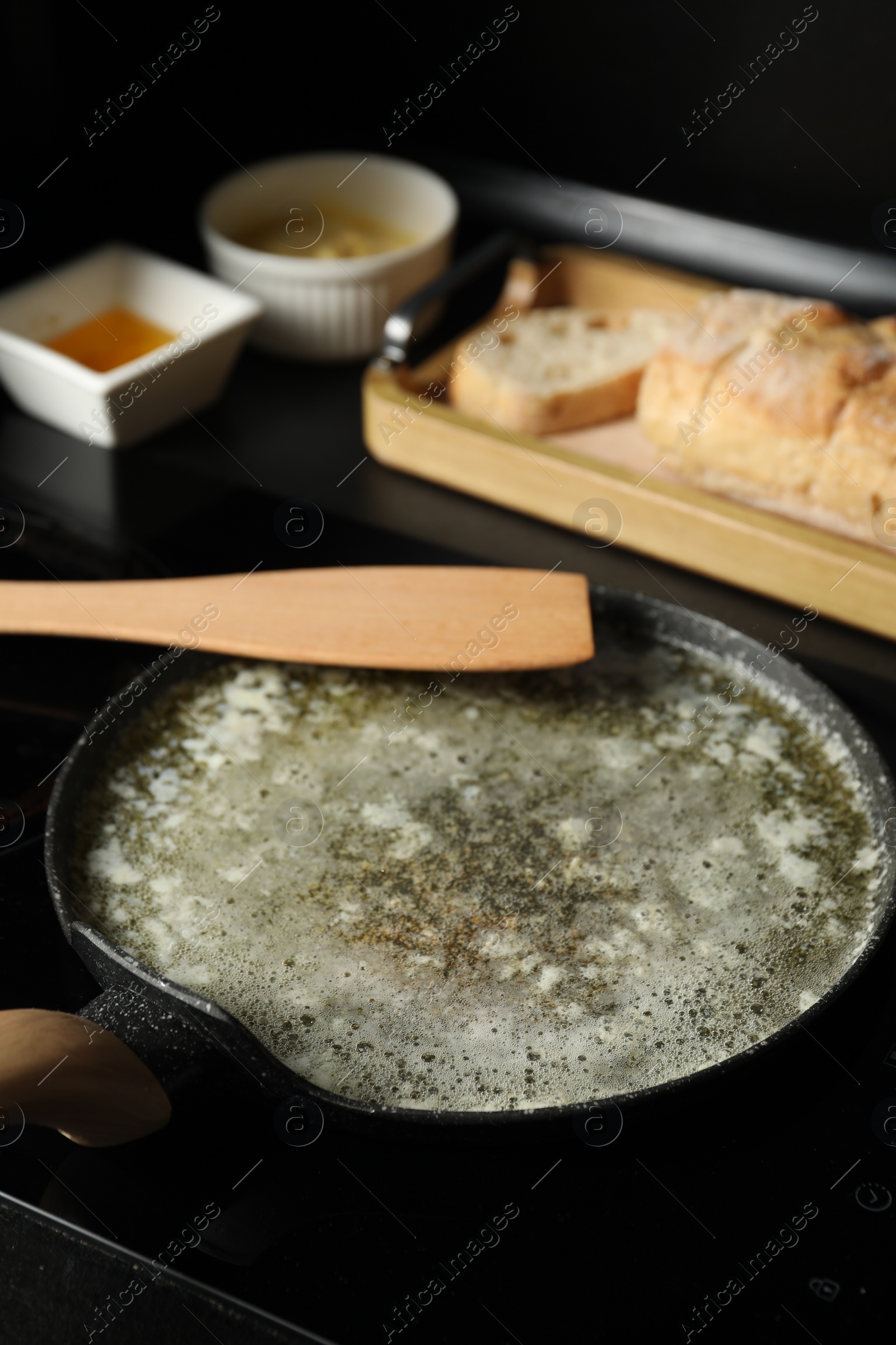 Photo of Melted butter in frying pan and wooden spatula on table