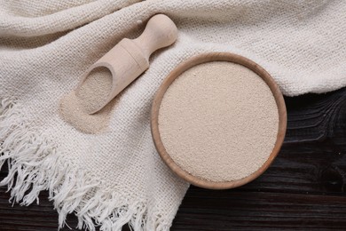 Bowl and scoop with active dry yeast on wooden table, top view