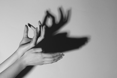Photo of Shadow puppet. Woman making hand gesture like deer on light background, closeup with space for text. Black and white effect