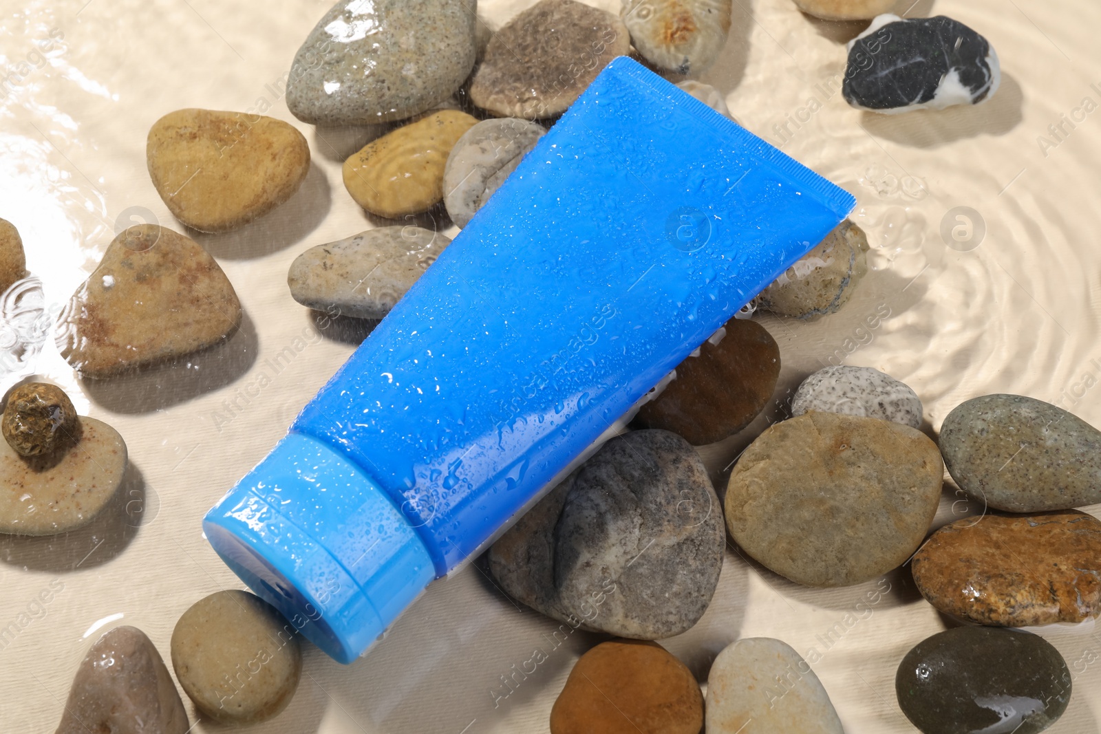 Photo of Tube of face cleansing product and stones in water against beige background, closeup