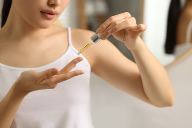 Beautiful young woman applying cosmetic serum onto her finger in bathroom, closeup