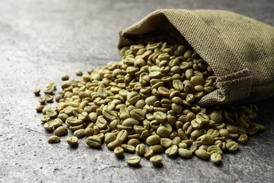 Photo of Overturned sackcloth bag with green coffee beans on grey table, closeup