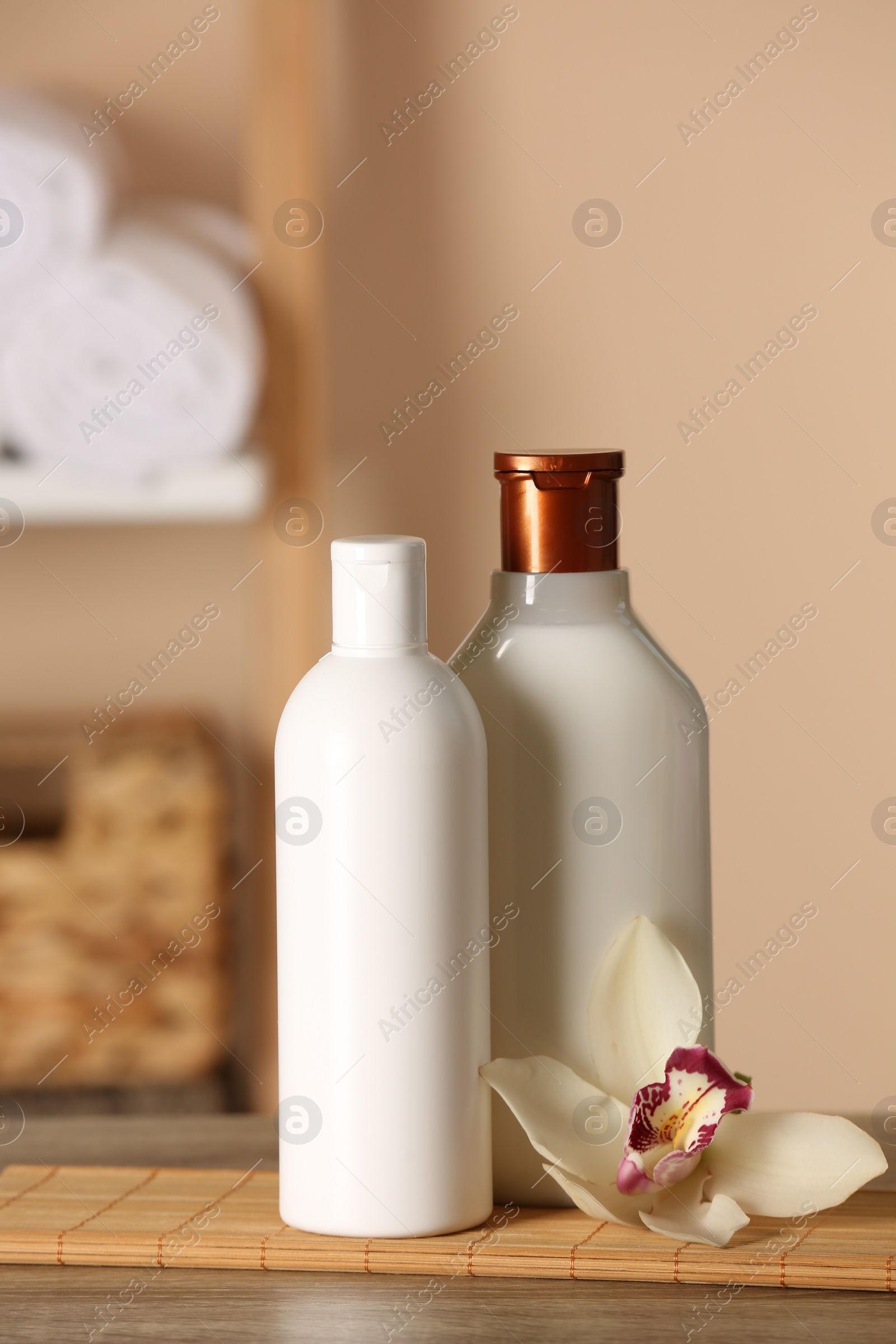 Photo of Bottles of shampoo and flower on wooden table in bathroom