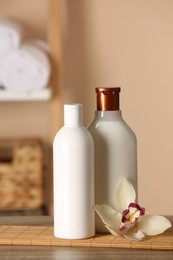 Photo of Bottles of shampoo and flower on wooden table in bathroom
