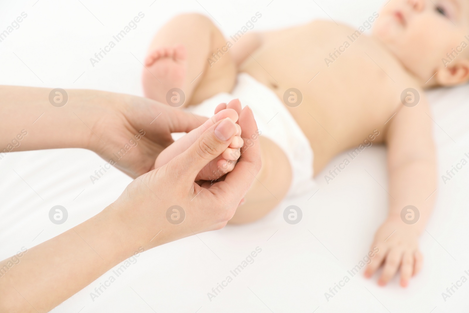 Photo of Mother and her cute child on white bed, closeup. Baby massage and exercises