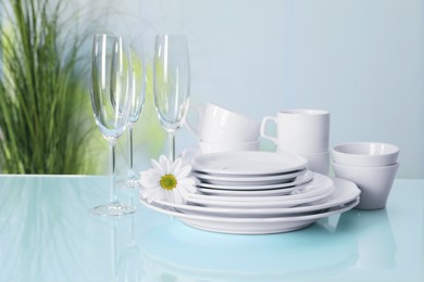 Set of clean dishware and flower on light blue table