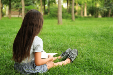 Photo of Cute little girl reading book on green grass in park