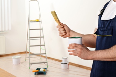 Photo of Male decorator with brush and paint can in empty room, closeup. Space for text