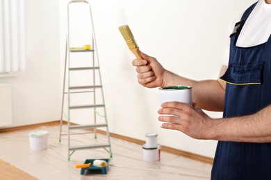 Male decorator with brush and paint can in empty room, closeup. Space for text