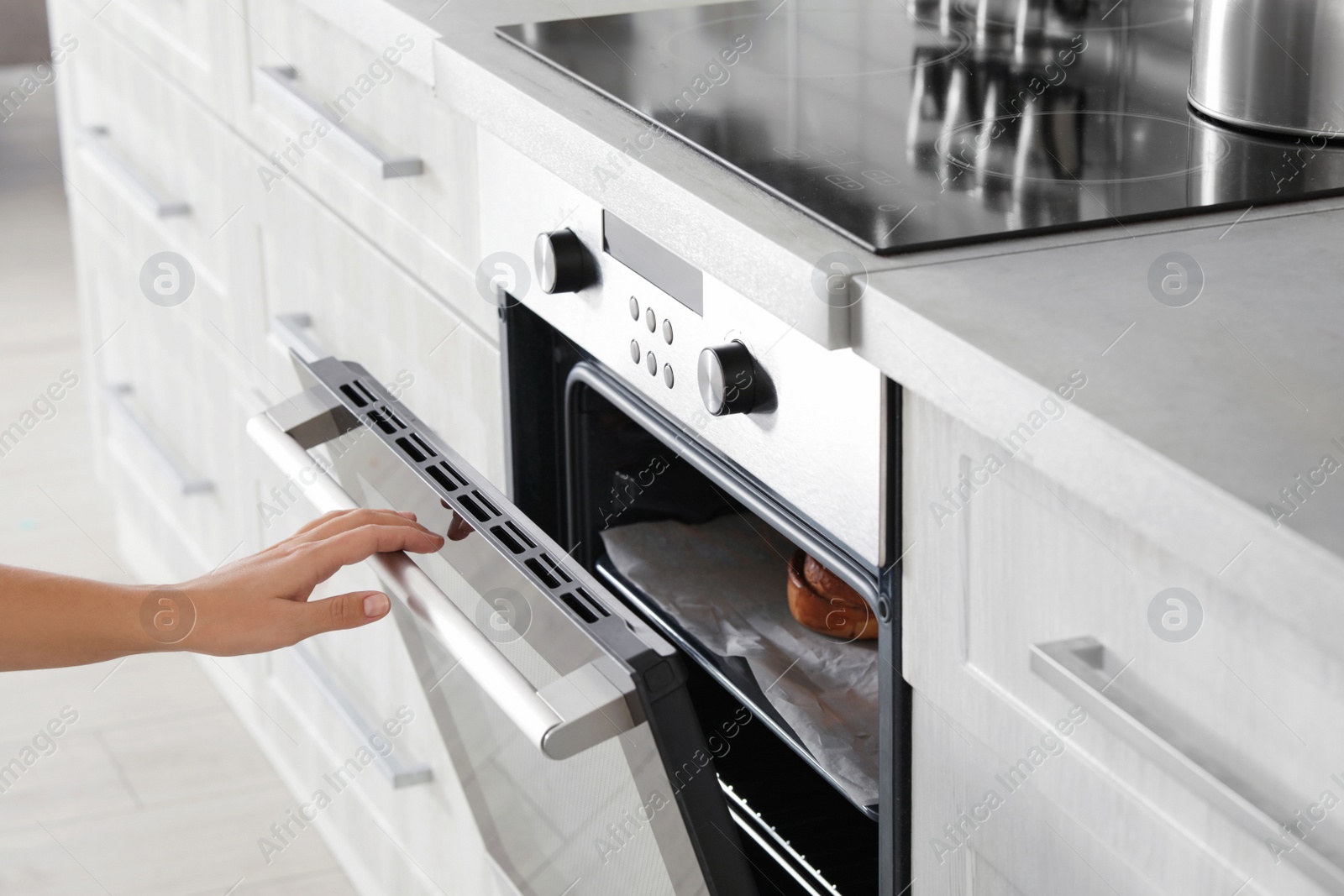 Photo of Young woman opening electric oven in kitchen, closeup