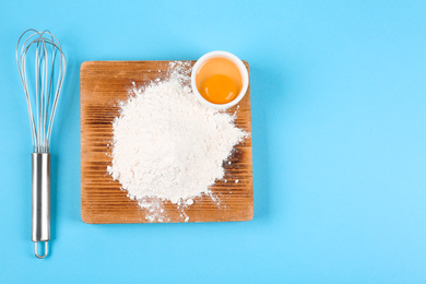 Photo of Raw eggs, whisk and flour on light blue background, flat lay. Baking pie