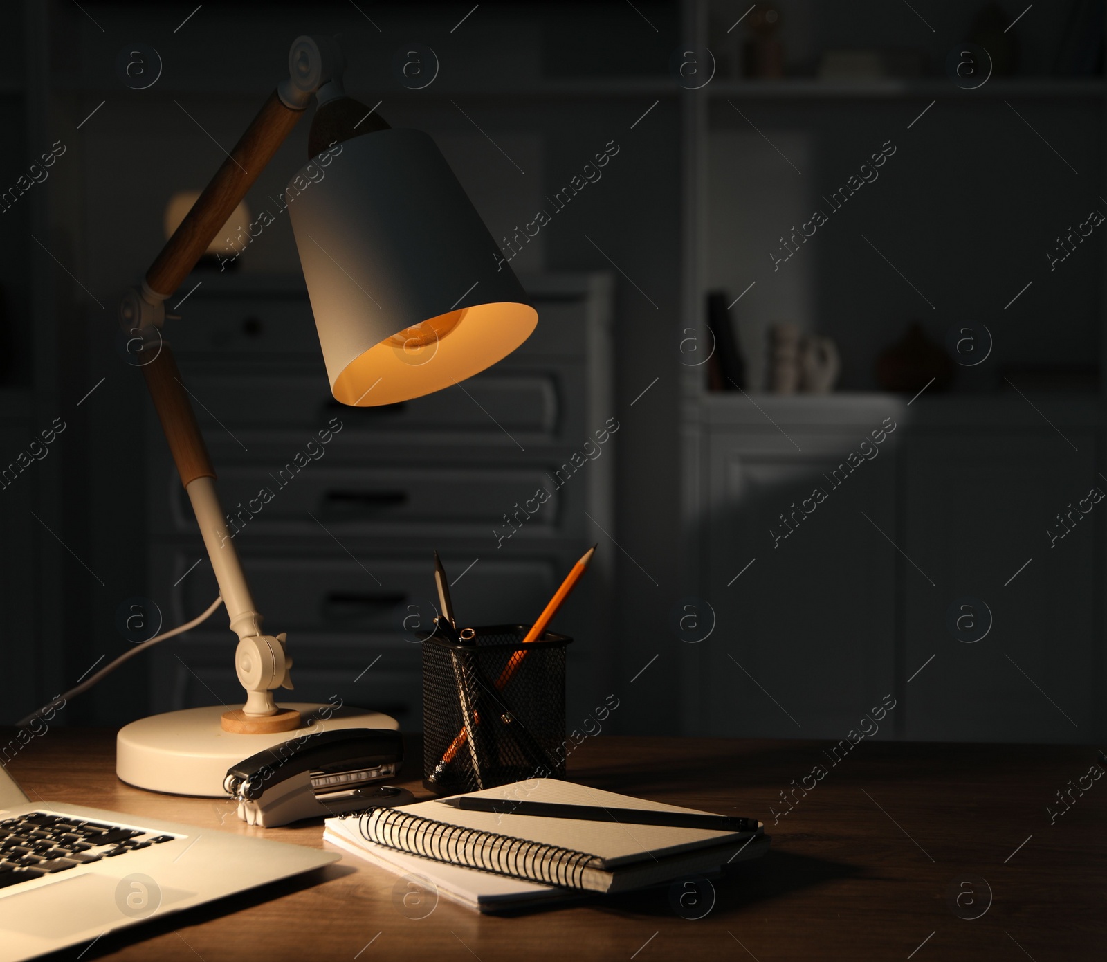 Photo of Stylish lamp and stationery on wooden table indoors. Space for text