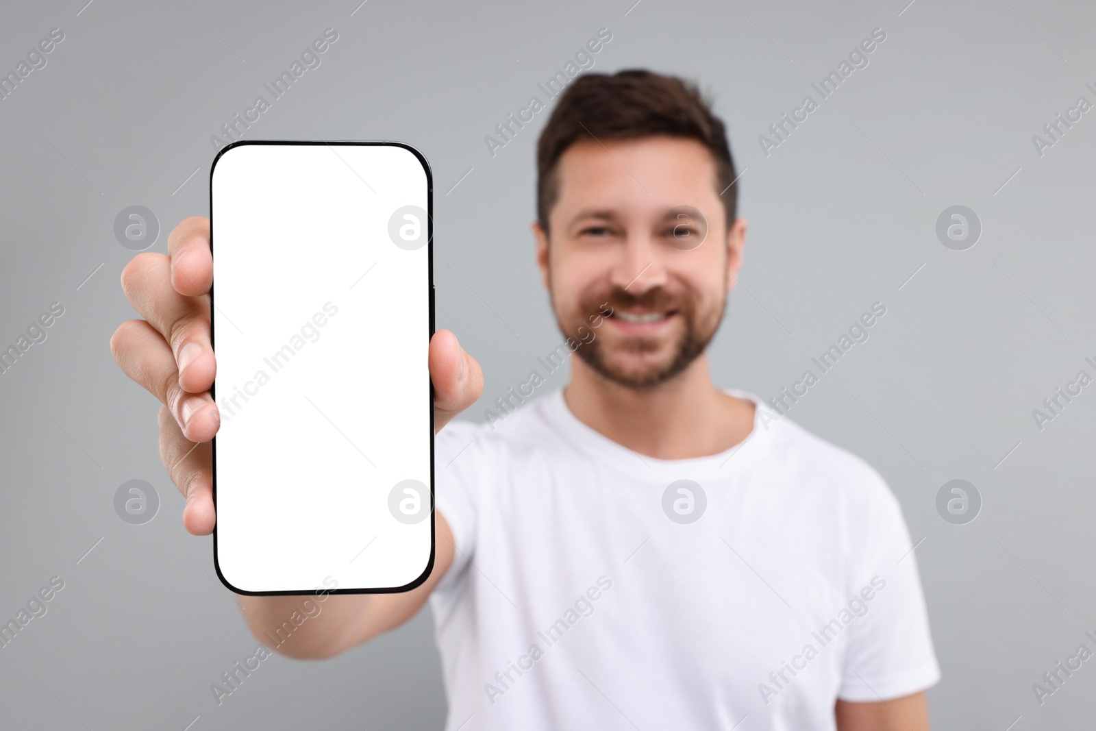 Photo of Handsome man showing smartphone in hand on light grey background, selective focus. Mockup for design