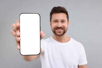 Photo of Handsome man showing smartphone in hand on light grey background, selective focus. Mockup for design