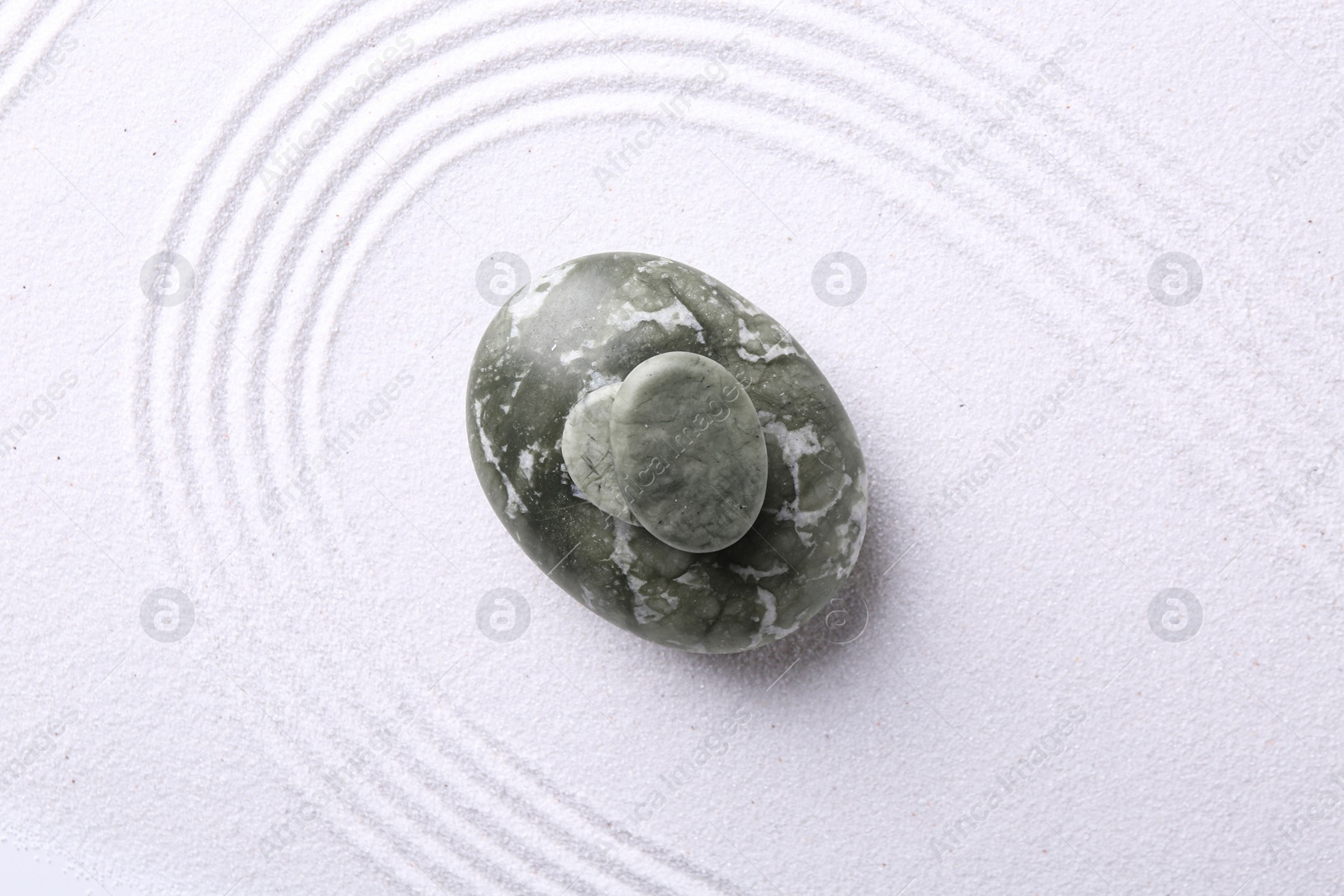 Photo of Zen garden stones on white sand with pattern, top view