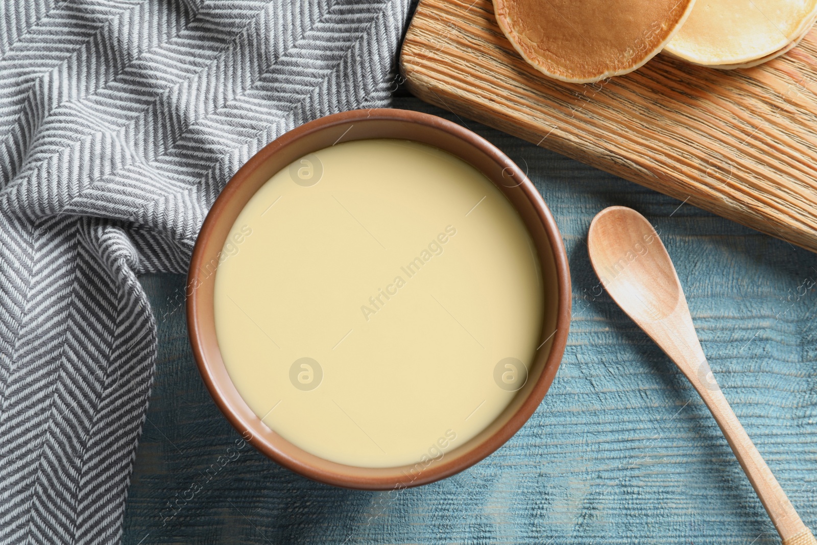 Photo of Bowl of condensed milk served on wooden table, top view. Dairy products